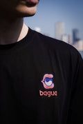 Person wearing a black t-shirt with an embroidered Bagua logo and text, set against a city skyline.